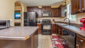 A kitchen with dark wooden cabinets, a stainless steel refrigerator, a microwave, a stove, and a dishwasher. - The Strickland Stopover (Fayetteville)