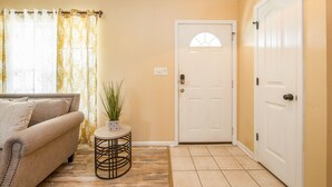 A hallway with a beige door, a small round table with a plant, and a sofa with cushions. - The Strickland Stopover (Fayetteville)