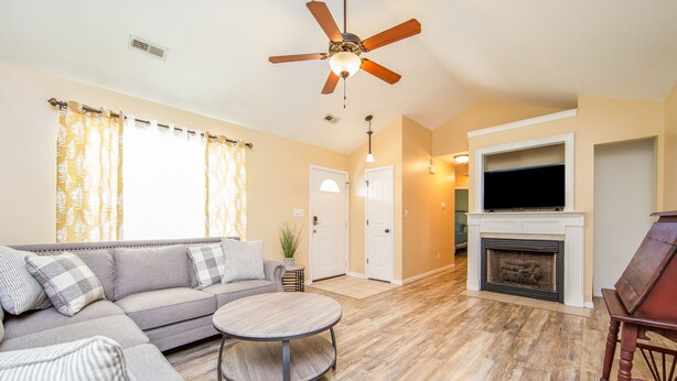 A living room with a sofa, coffee table, fireplace, TV, and ceiling fan. - The Strickland Stopover (Fayetteville)