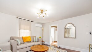 A living room with a beige sofa, a round wooden coffee table, a mirror, and a ceiling light fixture. - The Ramsey Rose Residence (Fayetteville)