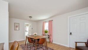 A dining area with a wooden table and chairs, a small rug, and a window with pink curtains. - The Ramsey Rose Residence (Fayetteville)