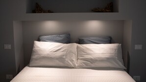 A bedroom with a bed, two pillows, and a shelf above the bed. - acquabianca plus (Catania)