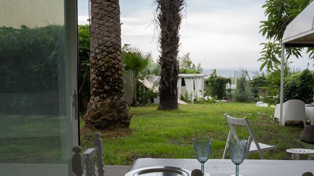 An outdoor dining area with a table set for two, overlooking a grassy garden and a view of the sea. - acquabianca plus (Catania)