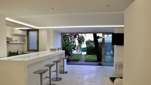A modern kitchen with a bar area, a TV mounted on the wall, and a view of the garden through the glass door. - acquabianca plus (Catania)