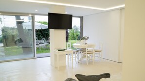 A modern living room with a white sofa, a flat-screen TV mounted on a wall, and a dining area with white furniture. - acquabianca plus (Catania)
