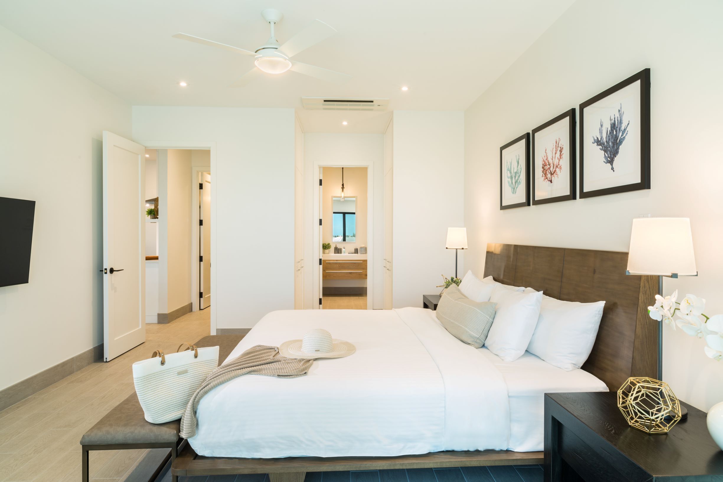 A modern hotel room with a large bed, bedside lamps, a flat-screen TV, and framed artwork on the wall.