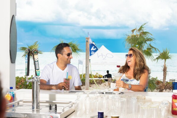 A bar area with a view of the beach, a flag, and a tent in the background. - H2O Life. Style. Resort. (Providenciales)