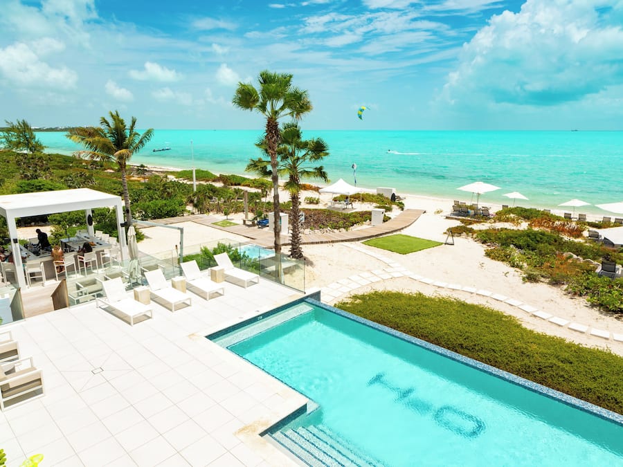 Un área de piscina con sillones de descanso, un espacio de estar cubierto y vistas a la playa y al océano.