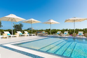A swimming pool with lounge chairs and umbrellas, surrounded by greenery. - H2O Life. Style. Resort. (Providenciales)