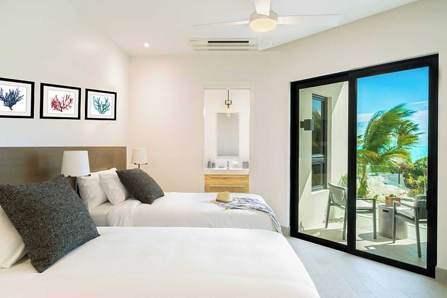 Habitación de hotel con dos camas, baño y balcón con vista al océano.