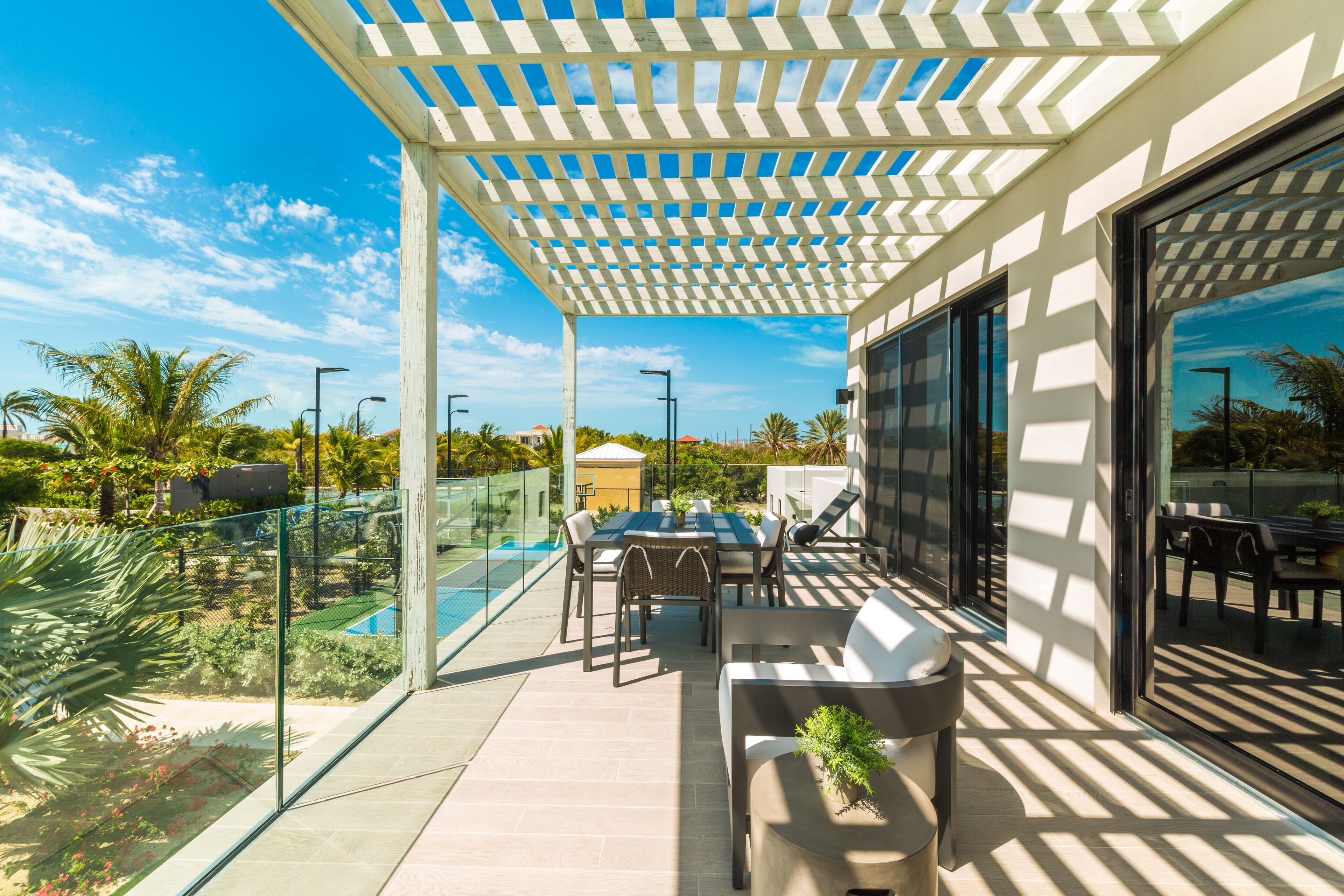 Un patio techado al aire libre con mesa y sillas, una parrilla y vistas a una piscina y follaje.