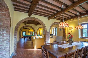 A spacious dining area with a wooden table and chairs, a brick fireplace, and a billiards table in the background. - Villa Montelopio (Peccioli)