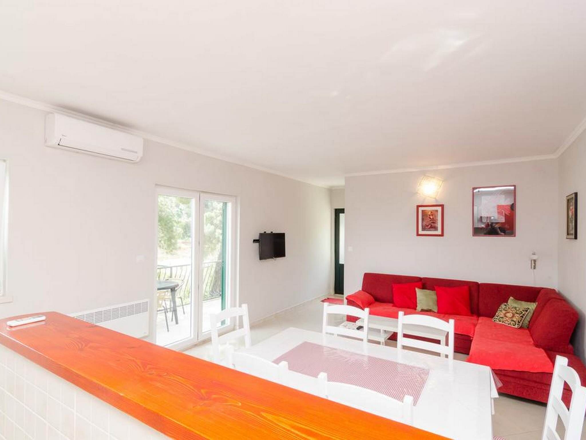 A bright living room with a red sofa, a white coffee table, and a glass-top dining table.