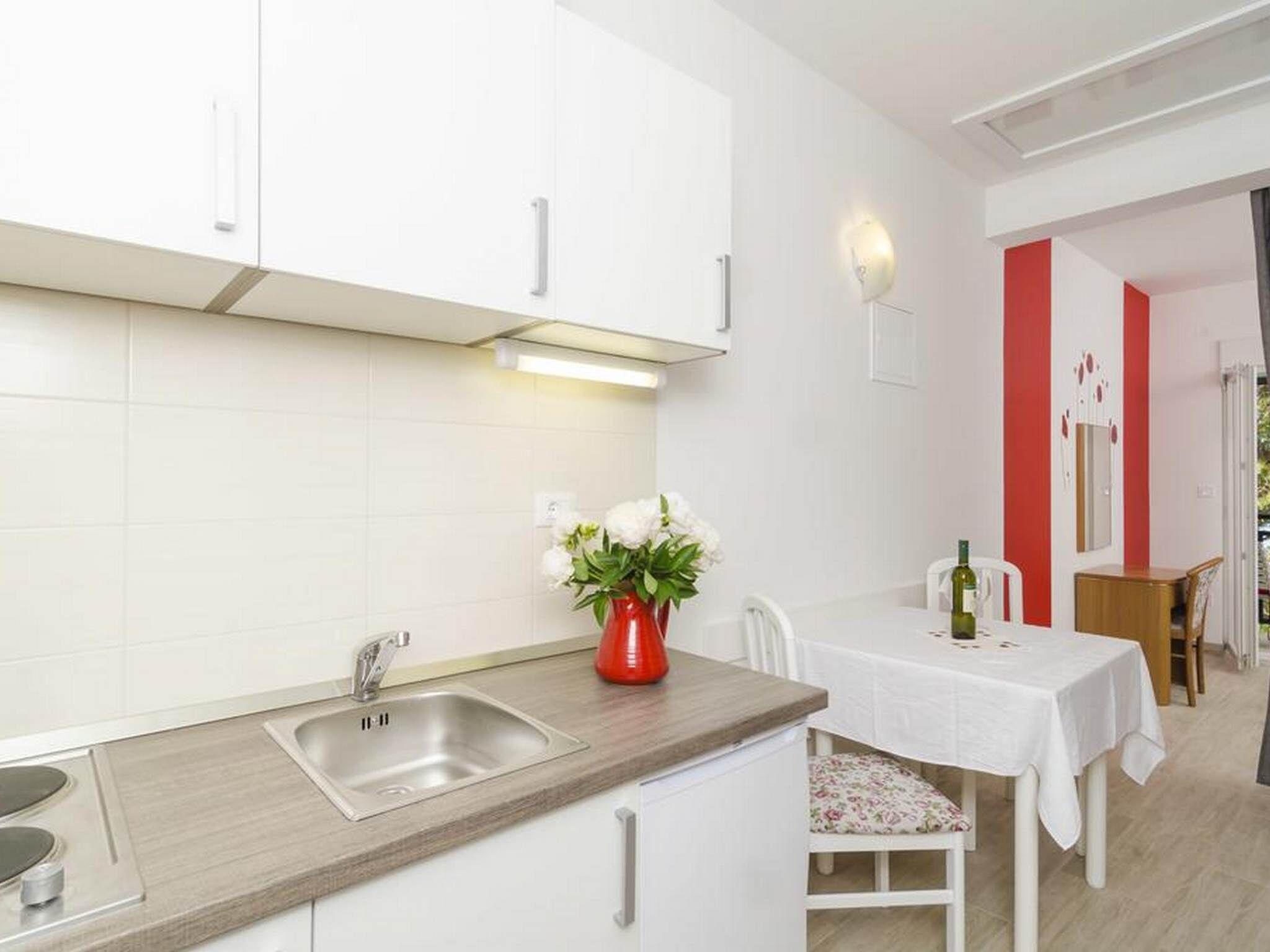 Una cocina moderna con armarios blancos, un lavamanos de acero inoxidable y un comedor con mesa y sillas blancas.
