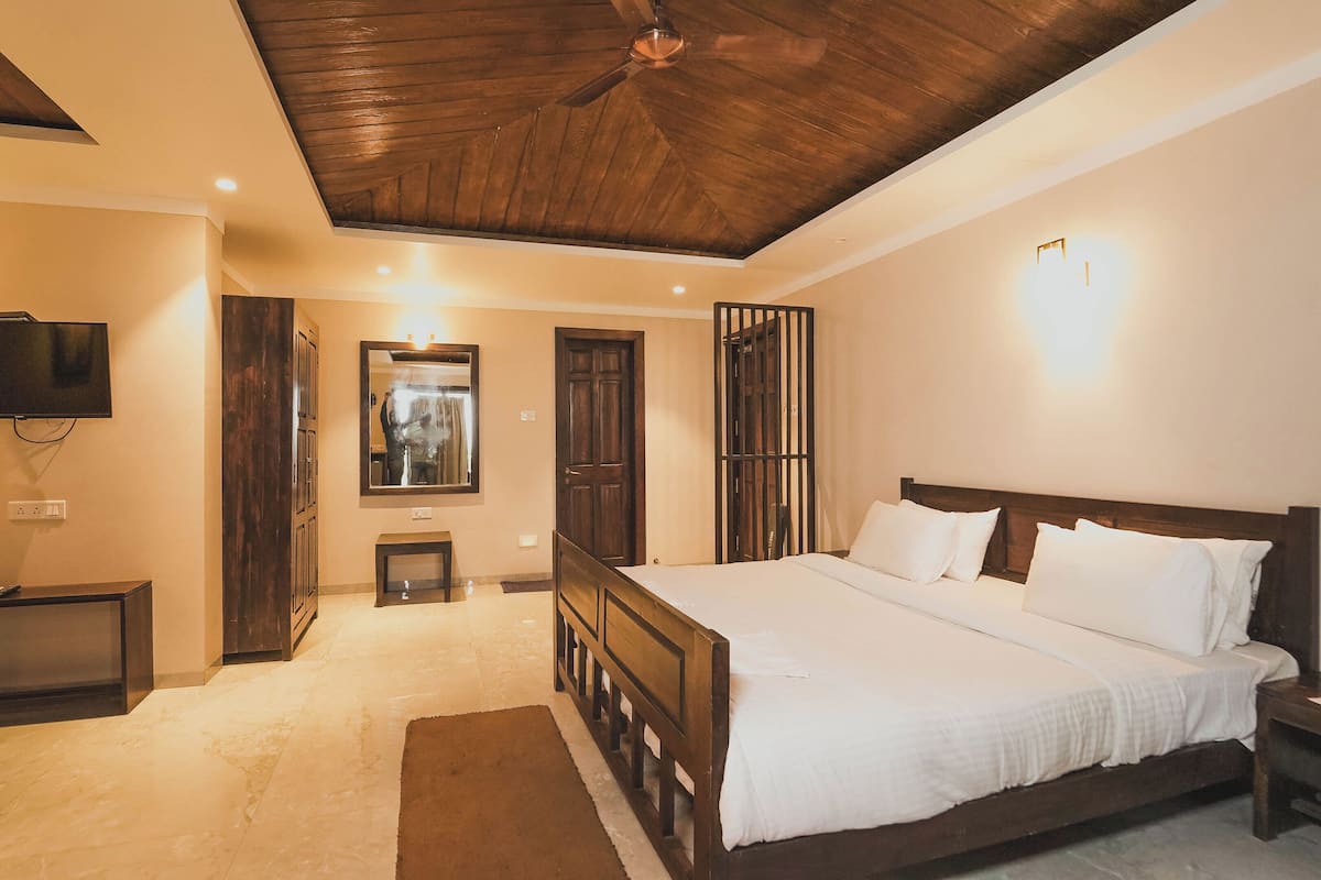 A bedroom with a wooden ceiling, a large bed, a TV, and a small table.