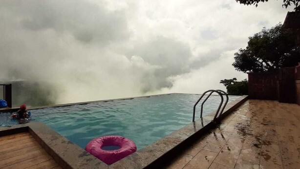 A swimming pool with a wooden deck, a metal ladder, and a pink floatation ring. - The Byke Sai Cottage, Mahabaleshwar (Satara)