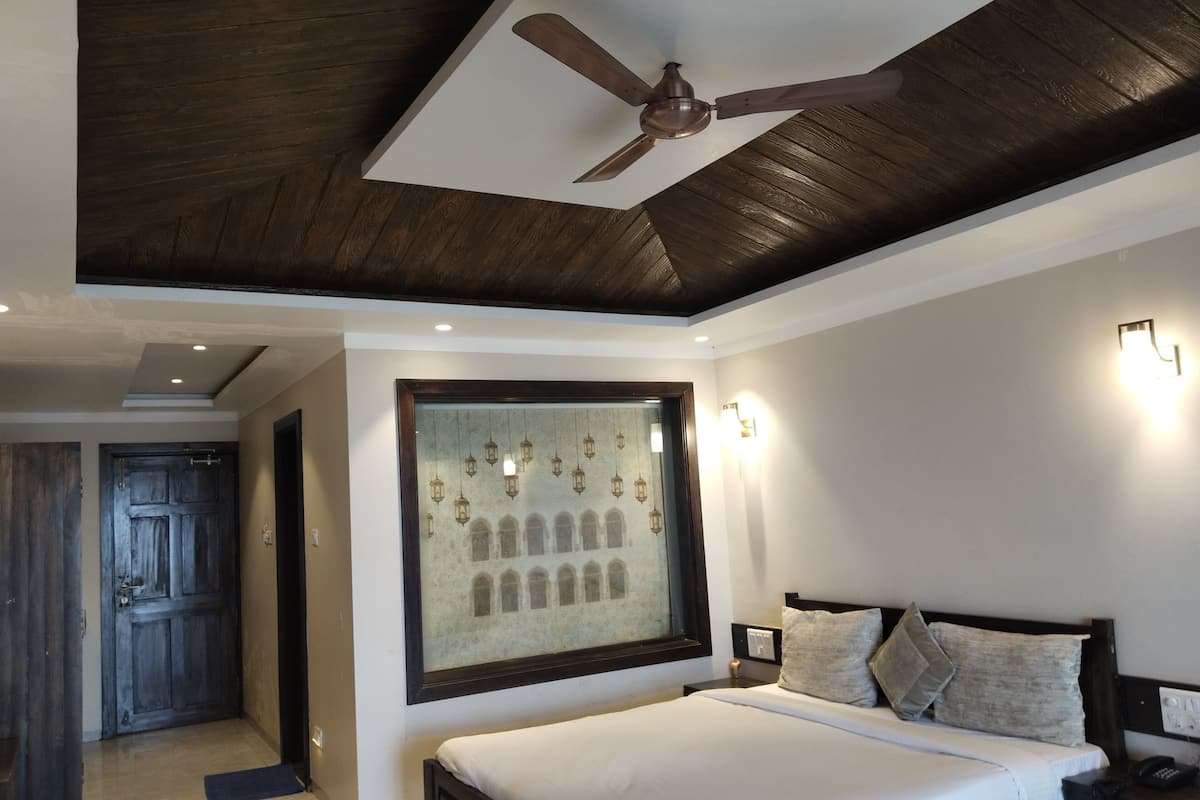 A bedroom with a large bed, a ceiling fan, a wall-mounted light fixture, and a framed picture on the wall.