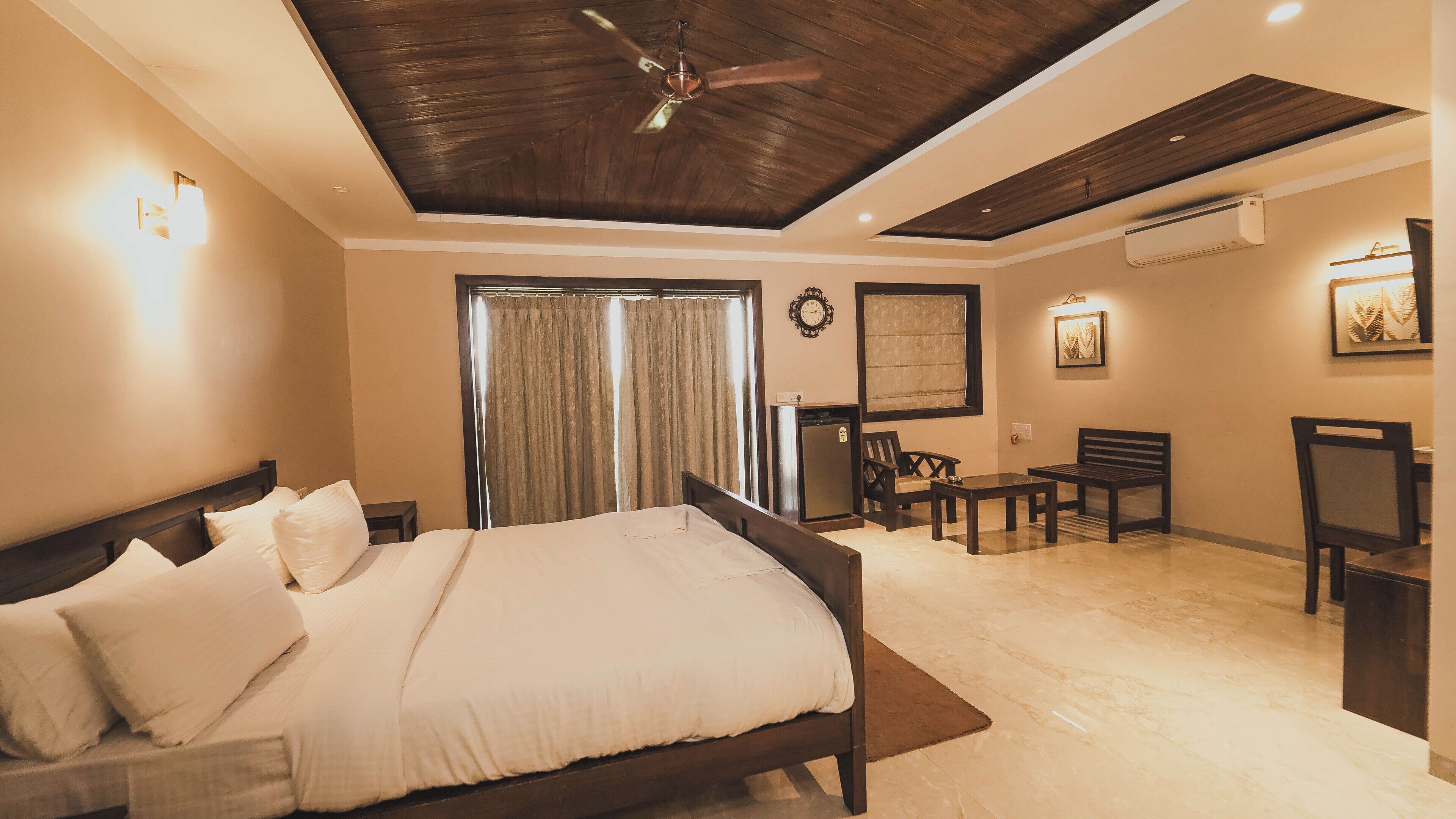 A hotel room with a bed, a ceiling fan, a desk, a chair, and a small table.