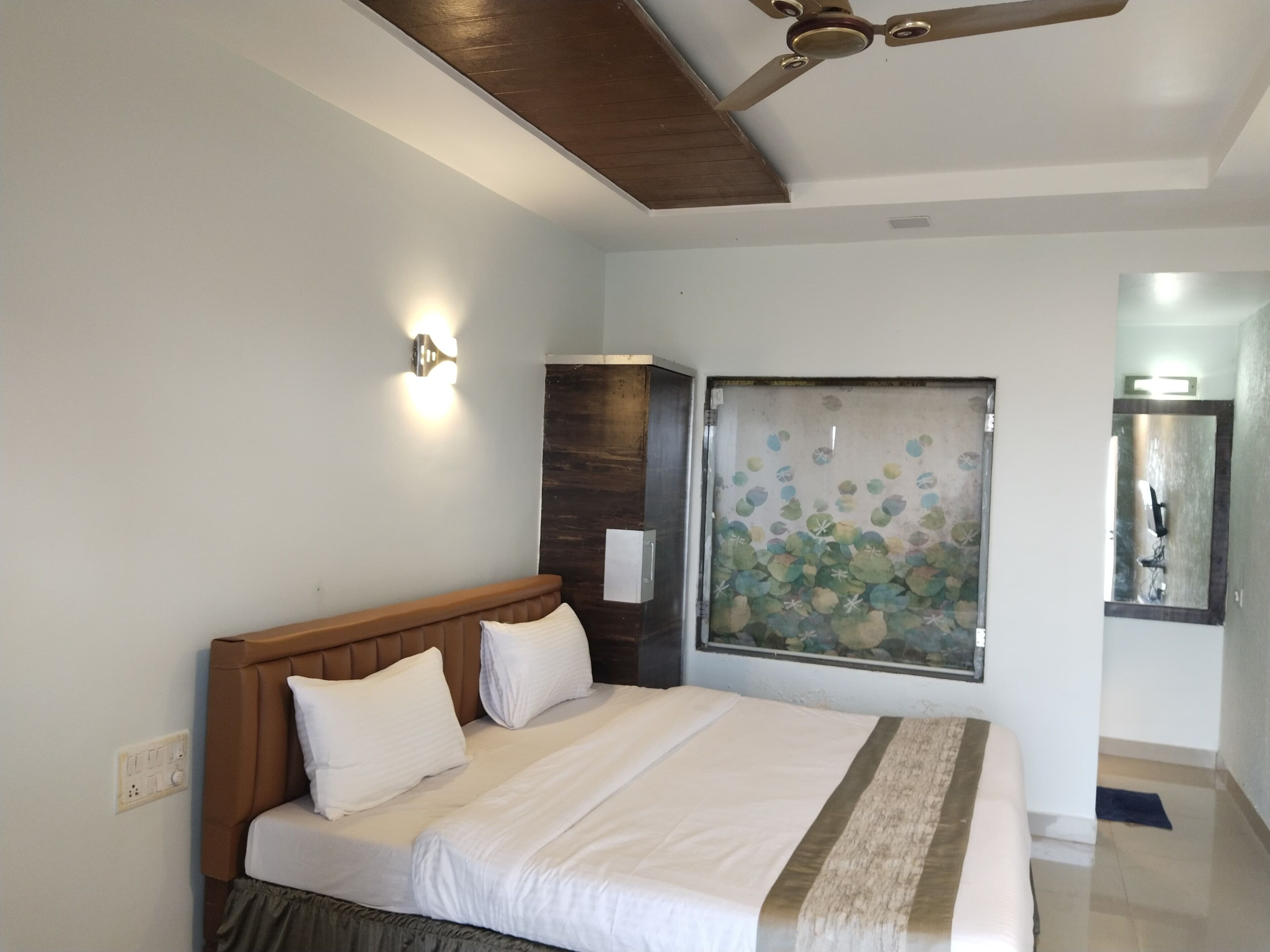 A bedroom with a bed, a ceiling fan, a wall-mounted light, and a decorative window treatment.