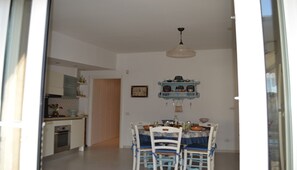 Un coin repas avec une table et des chaises, un luminaire suspendu et une cuisine en arrière-plan.