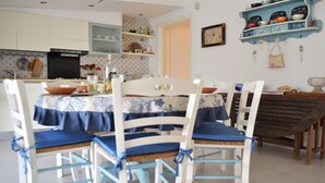 Comedor con una mesa dispuesta para cuatro personas, rodeada de sillas blancas con cojines azules.
