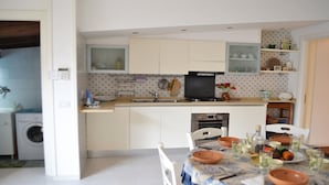 Cocina compacta con lavadora, comedor con mesa para dos personas y horno pequeño.