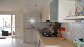 Una cocina con salpicadero de azulejos, estufa y lavamanos. Se ve una ventana con vista al exterior.