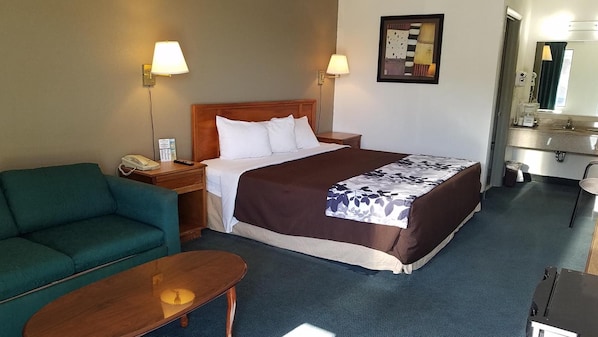 Ein Hotelzimmer mit einem Bett, einem grünen Sofa, einem Holztisch und einem kleinen Schreibtisch mit Lampe.