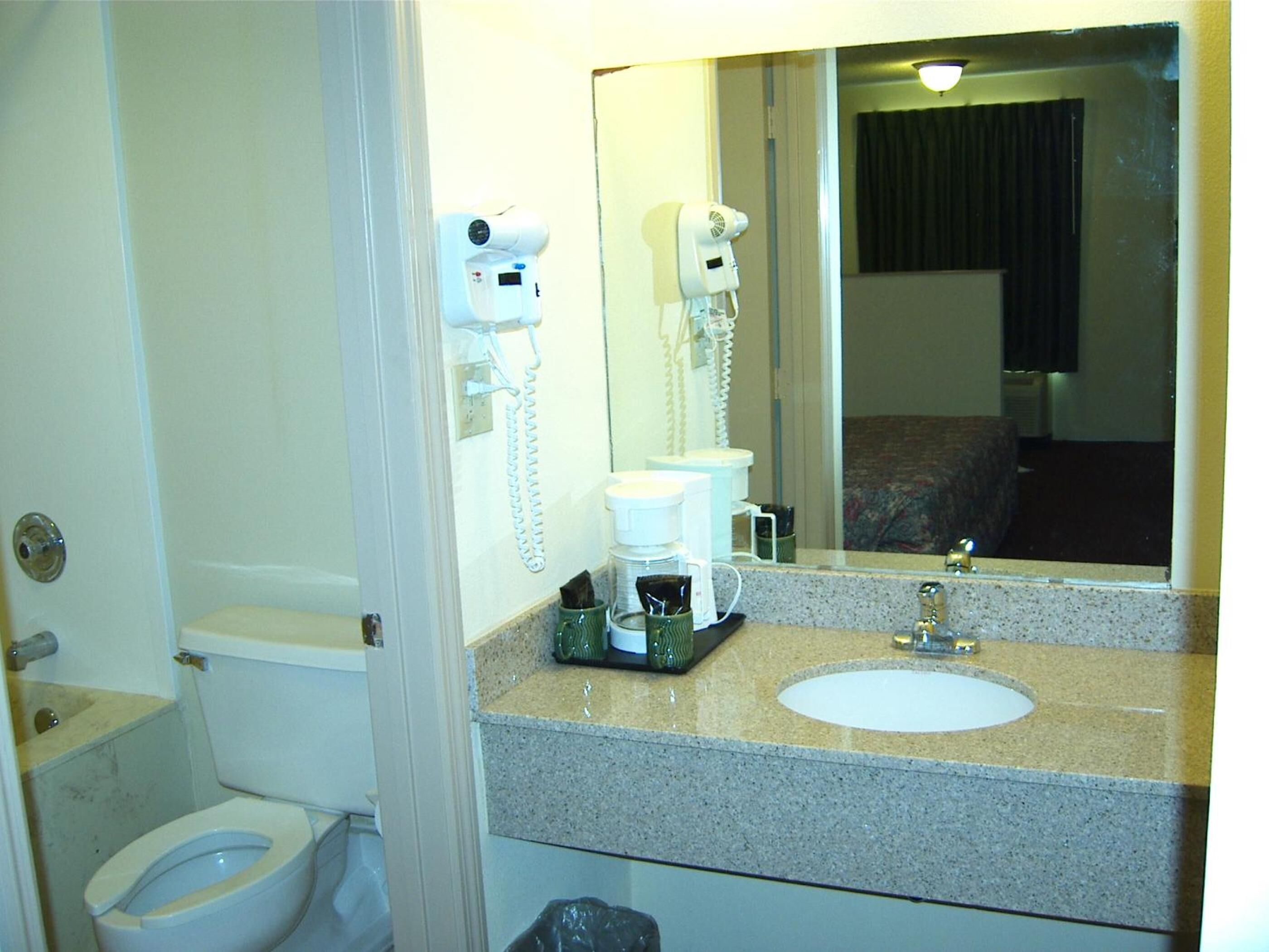 A bathroom with a toilet, a sink, a mirror, and a hairdryer mounted on the wall.