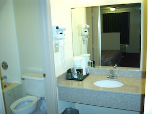 Un baño con inodoro, lavabo, espejo y secador de pelo fijado a la pared.