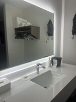 Un baño de hotel con un espejo grande, un lavamanos blanco y un perchero con toallas dobladas.