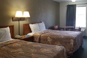 Habitación de hotel con dos camas, un escritorio, una silla y una ventana con cortinas.