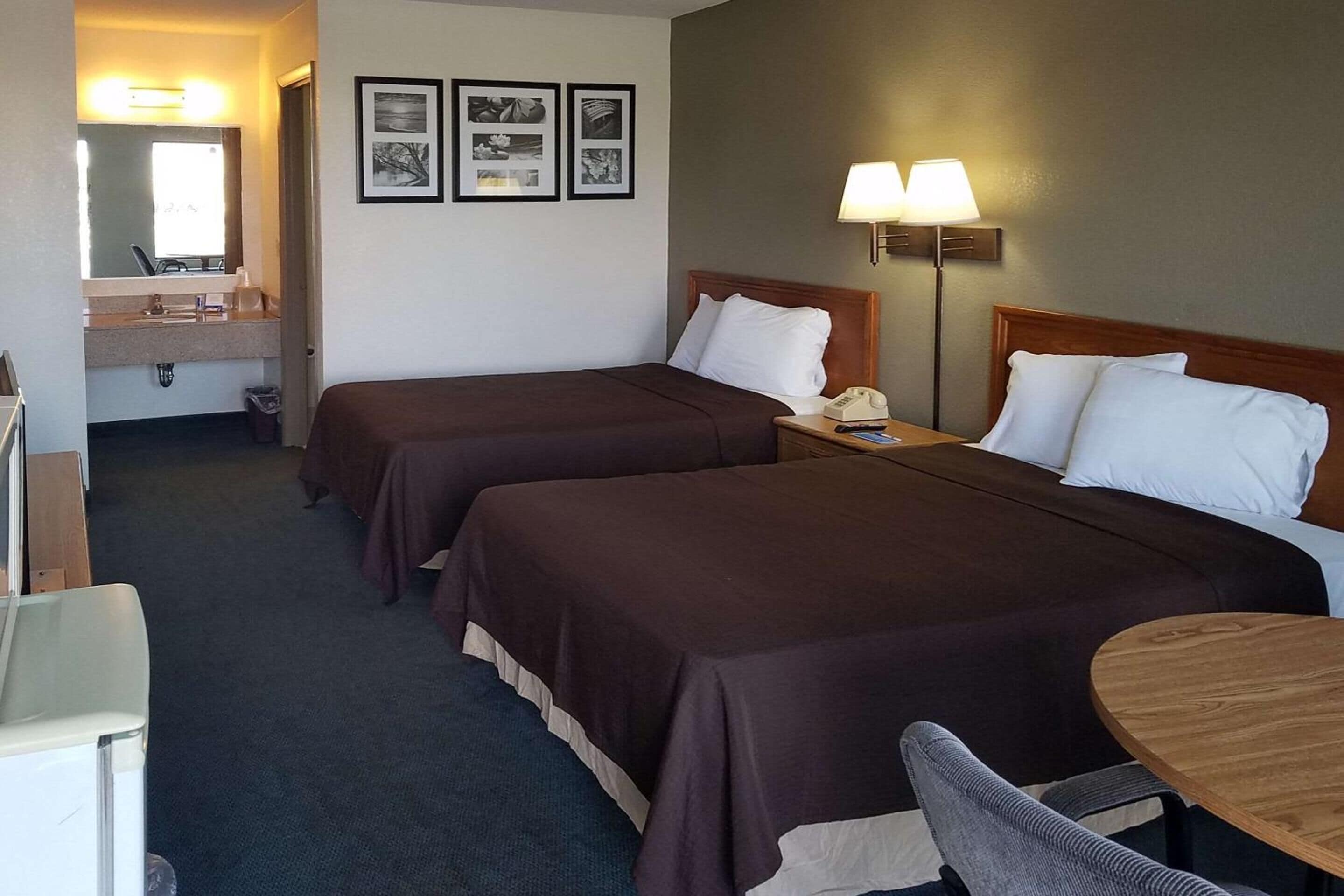 A hotel room with two beds, a desk, a chair, a lamp, and a mirror.