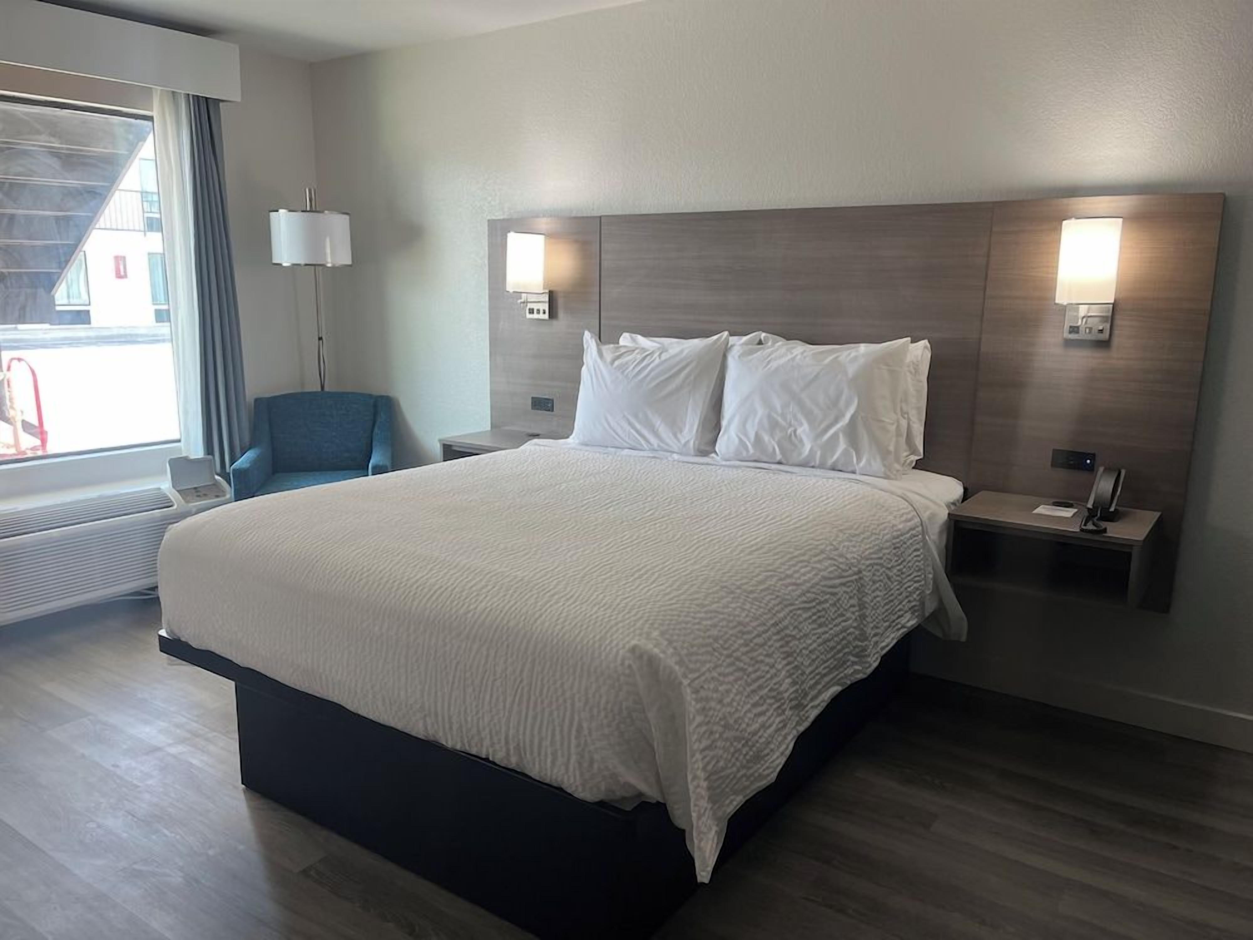 A hotel room with a large bed, bedside tables, a chair, and a window with curtains.