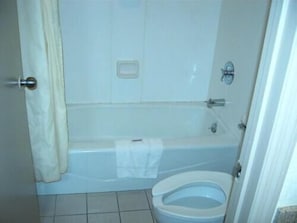 Un baño con bañera, inodoro y una toalla colgada en la pared.