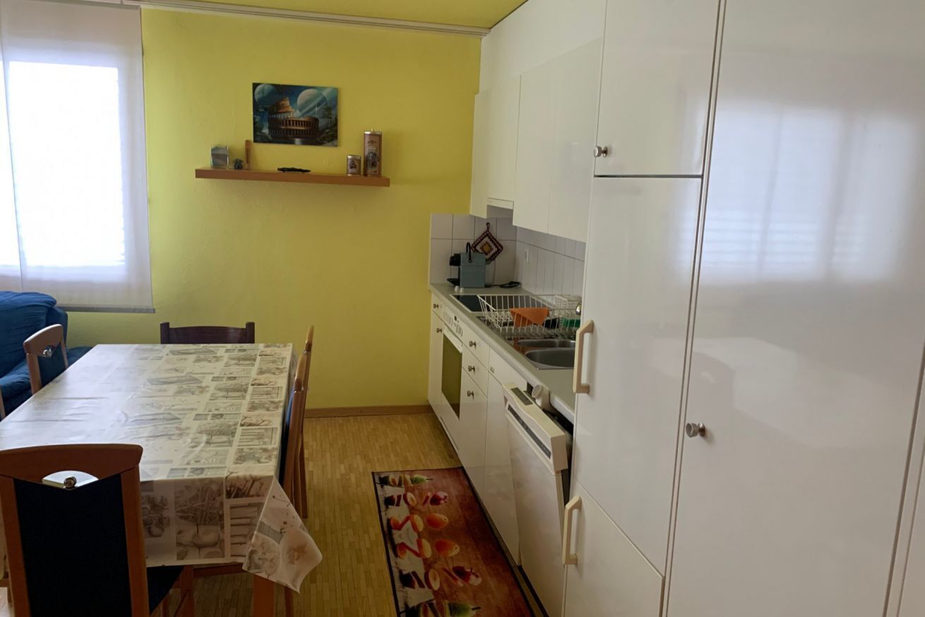 Eine kompakte Küche mit weißen Schränken, einem Esstisch mit Stühlen und einem kleinen Fenster.