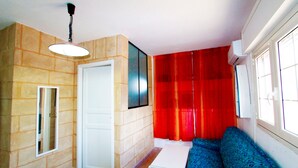 Una habitación con pared de piedra, una puerta blanca, un sofá azul, una mesita y una ventana con marcos blancos.