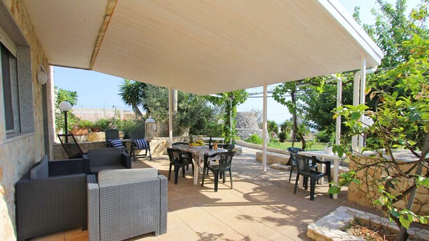 Un patio al aire libre con mobiliario de mimbre, una zona de estar cubierta y un muro de piedra.