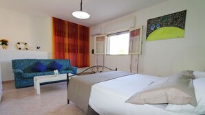 Un dormitorio con cama, sofá, una mesa de centro y una ventana con cortinas.