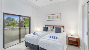 A bedroom with two beds, a balcony, and a framed artwork on the wall.