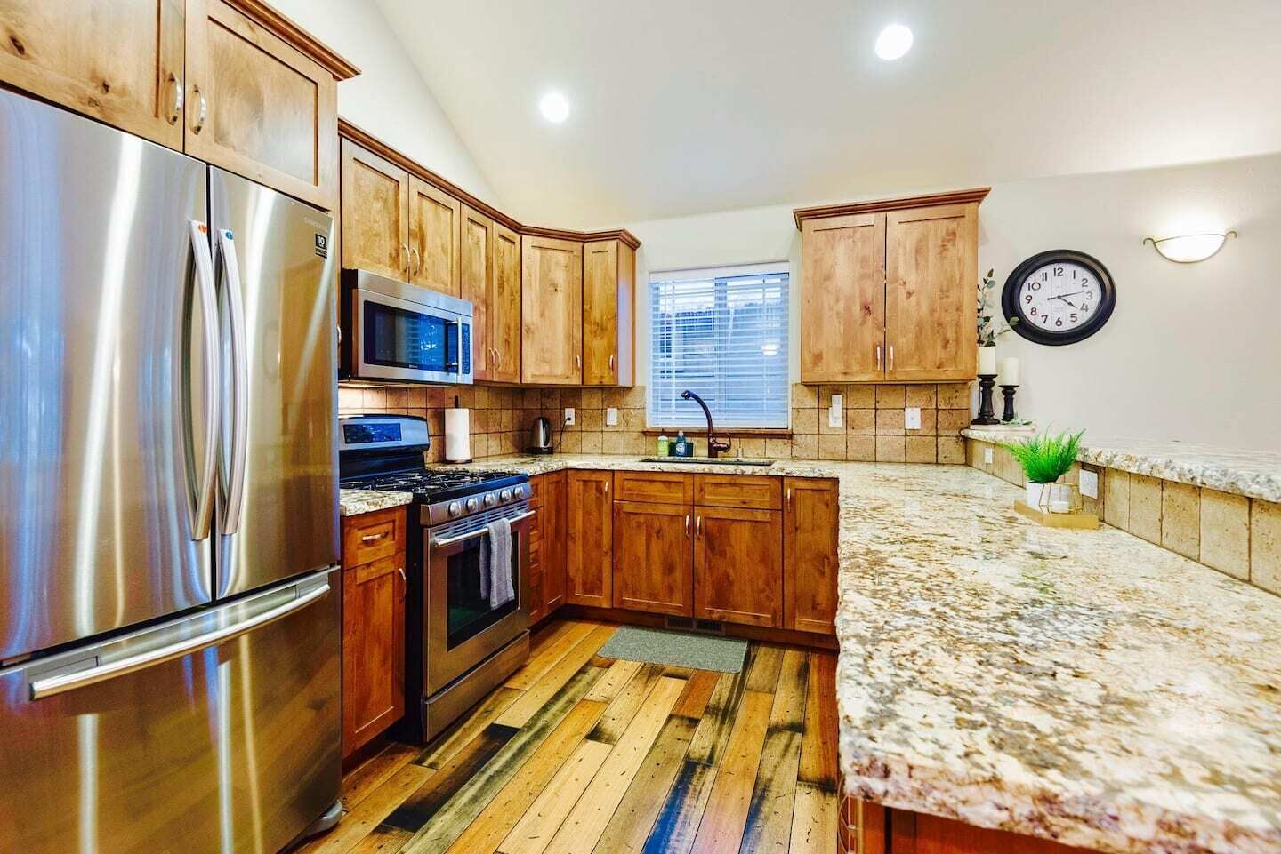 A kitchen with wooden cabinets, stainless steel appliances, a granite countertop, and a window with blinds.