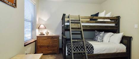 Una cama litera con escalera, una mesita de noche con lámpara y un ciervo montado enmarcado en la pared.