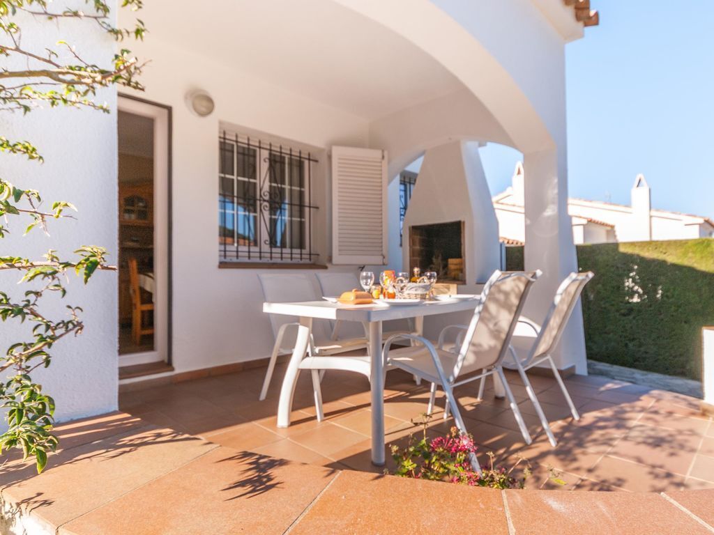 Un patio con una mesa lista para comer, rodeado de sillas y con vista a un edificio al fondo.