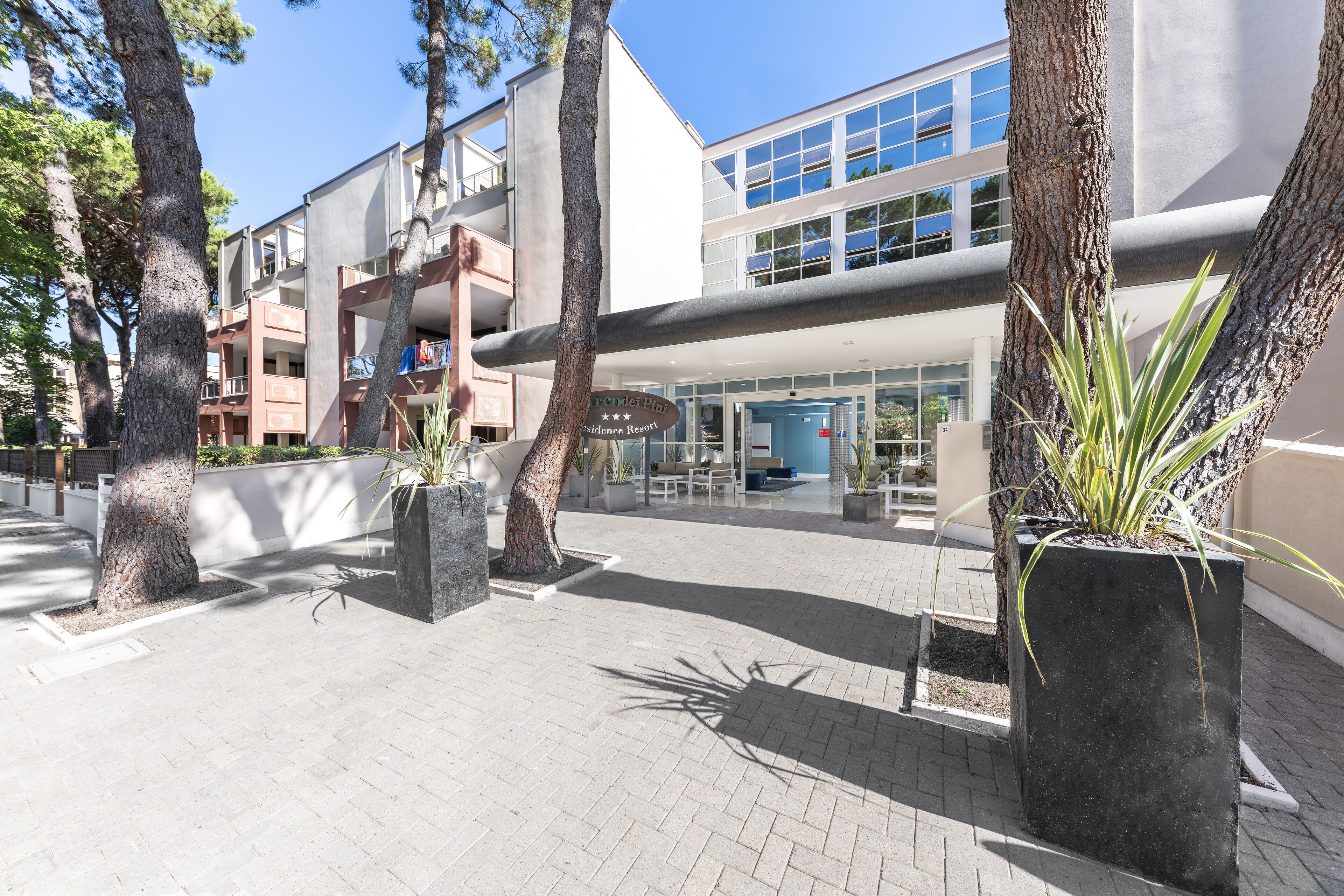 A modern building with a glass facade, surrounded by trees and potted plants.