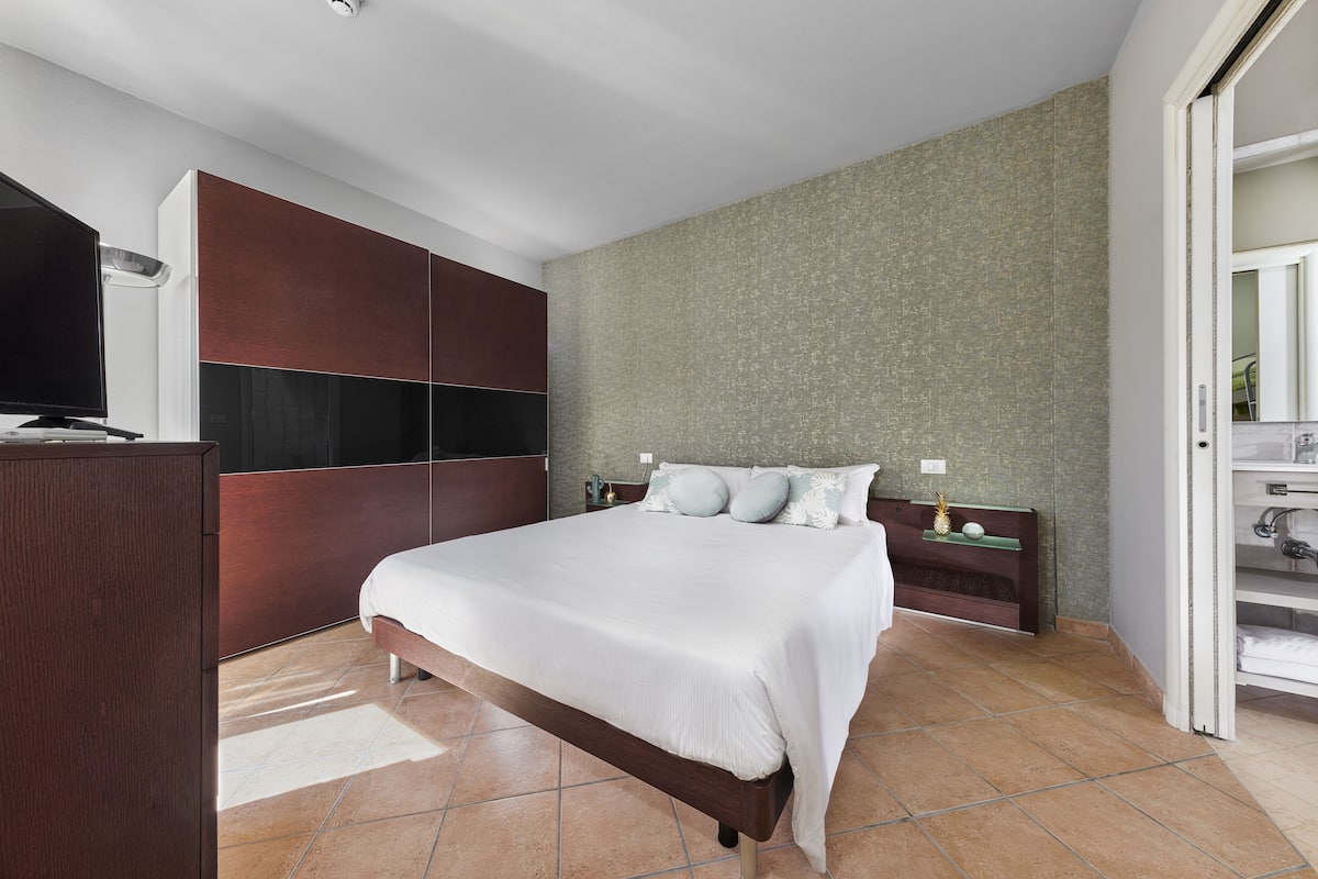 A modern bedroom with a large bed, built-in wardrobe, and a nightstand with a lamp.