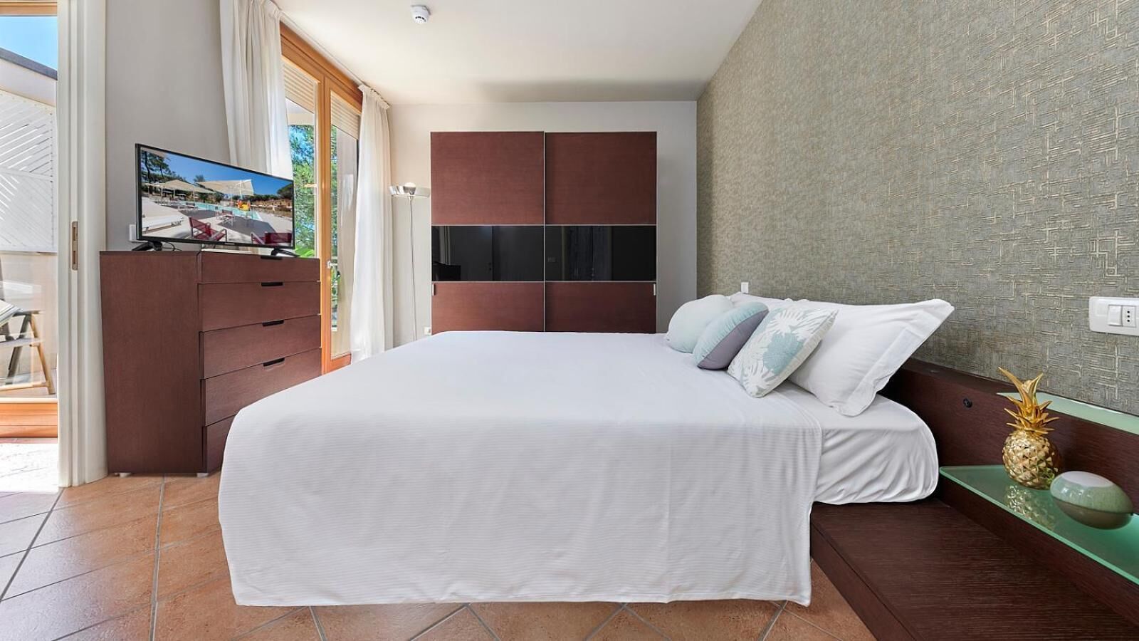 A bedroom with a bed, a TV, a wardrobe, and a view of an outdoor area.