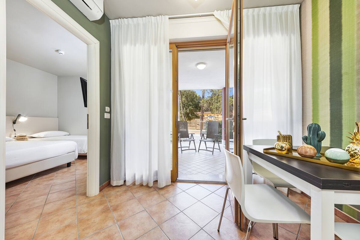 A hotel room with a bed, a desk with a tray of decorative items, and a view of the outdoor patio area.