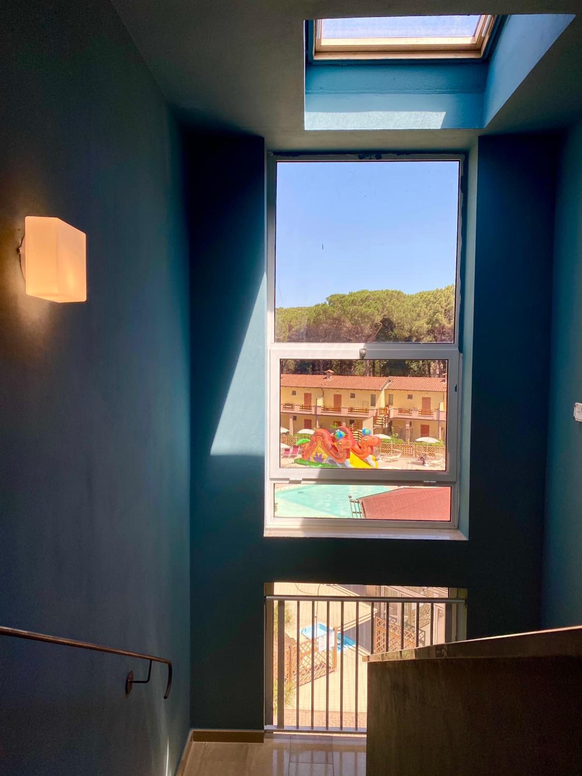 A room with a skylight, a large window, and a view of a building with a pool.