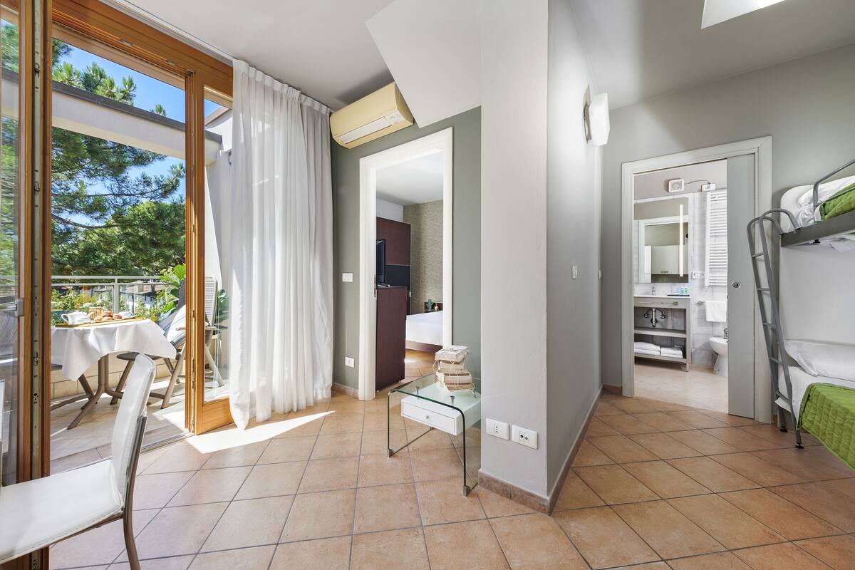 A hotel room with a balcony, a dining area, a bathroom, and a bed.