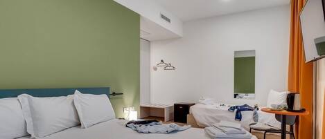 A hotel room with a large bed, a smaller bed, a desk, a chair, a mirror, and a TV.